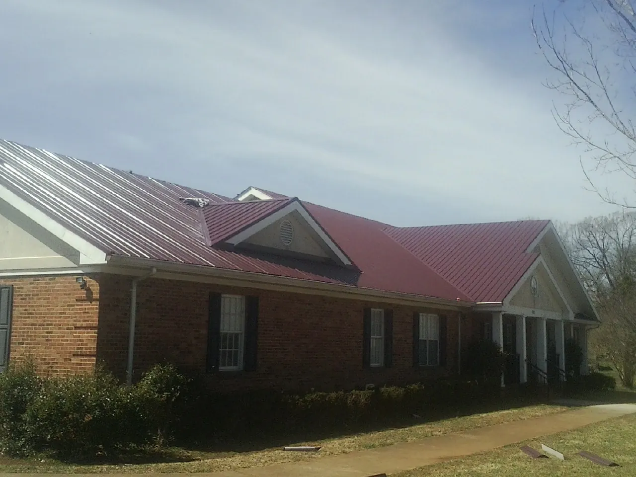 Red metal roof with gabled entries on a long brick building, from a Hail Damage Roof Repair job in Three Rivers