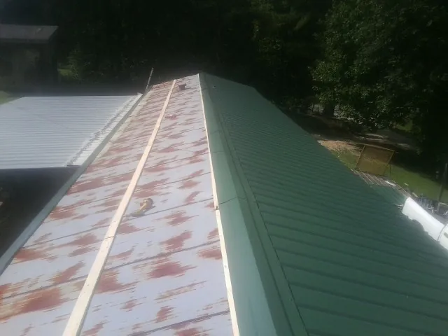 Old rusted panels beside newly installed green metal roofing — Wind Damage Roof Repair by Roofing Brothers in Three Rivers