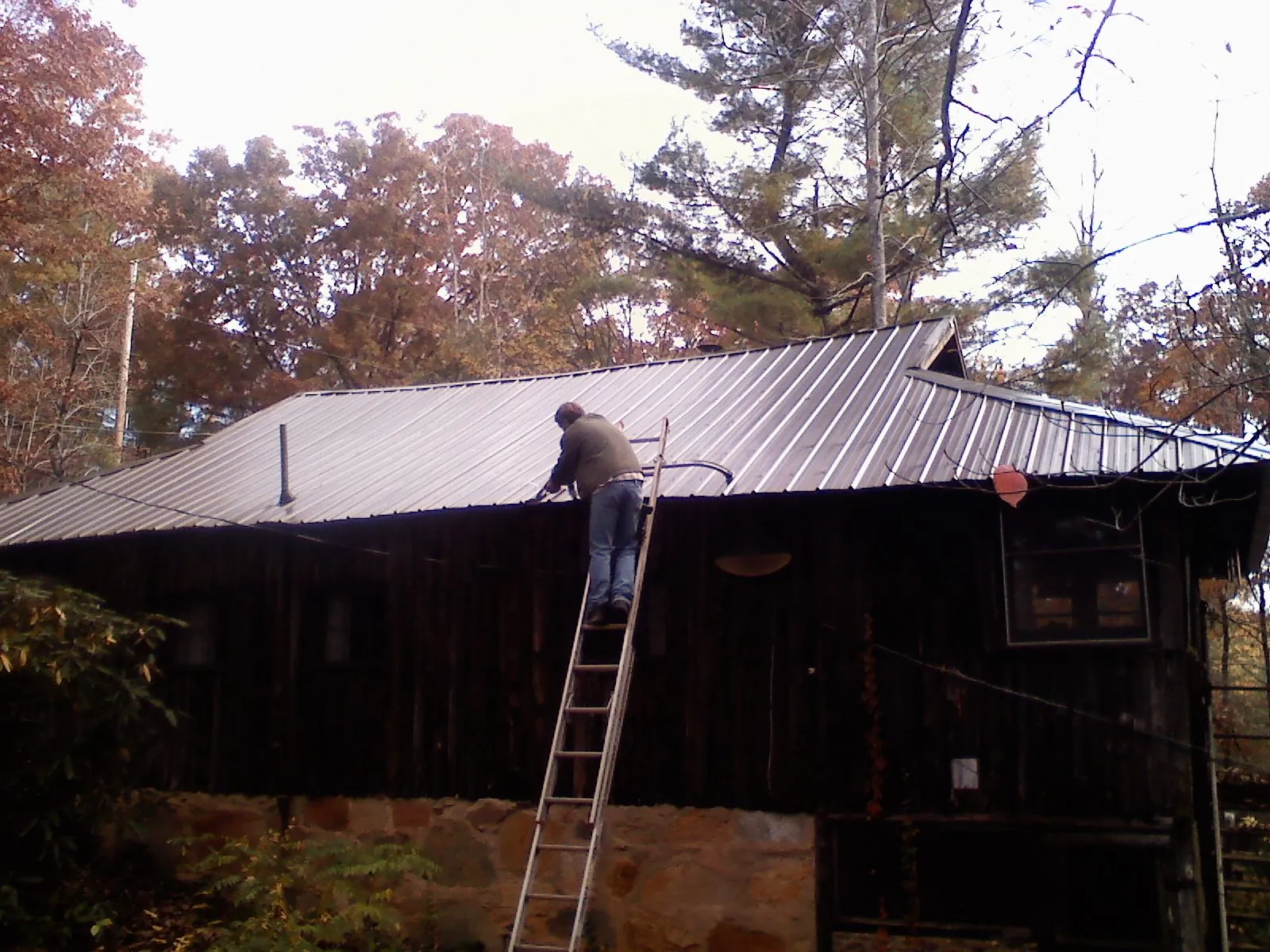 Roofer on a ladder working along the edge of a cabin metal roof in Three Rivers